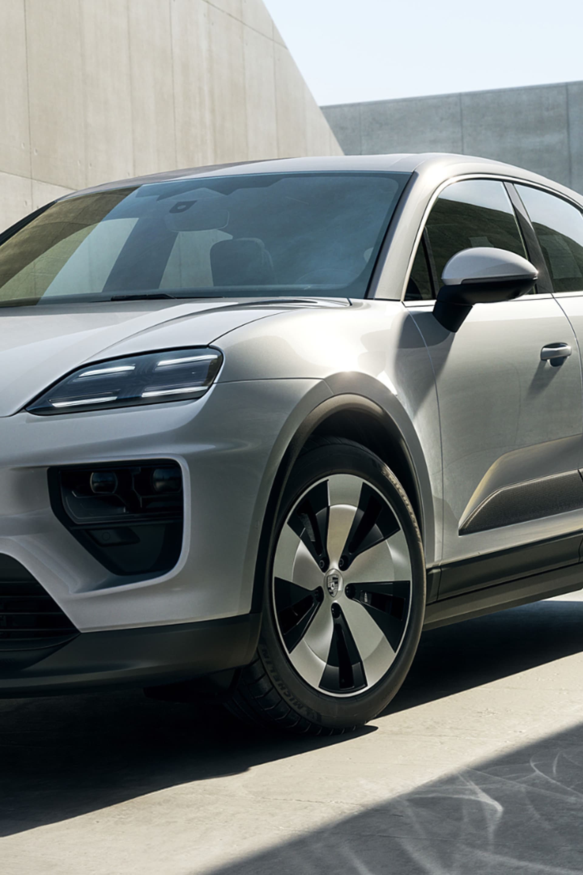 Porsche Macan 4 Ice Grey -metallisessa profiilissa betoniseinää vasten, jossa on LED-valot, nykyaikaiset linjat ja 20-tuumaiset turbiinikerrokset.